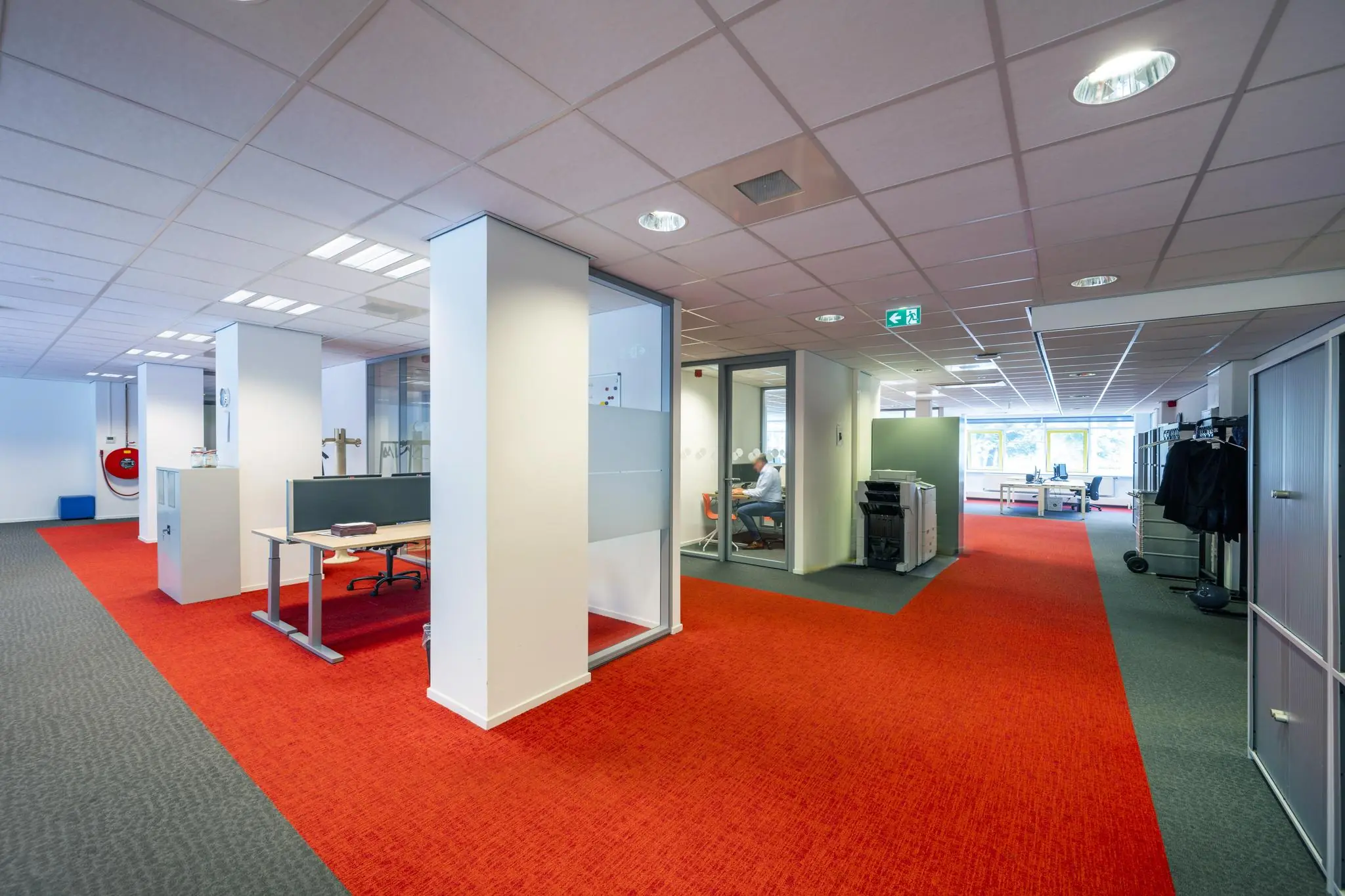 Modern kantoorinterieur aan de Jan Tooropstraat met open werkplekken, vergaderruimtes en rode vloerbedekking.